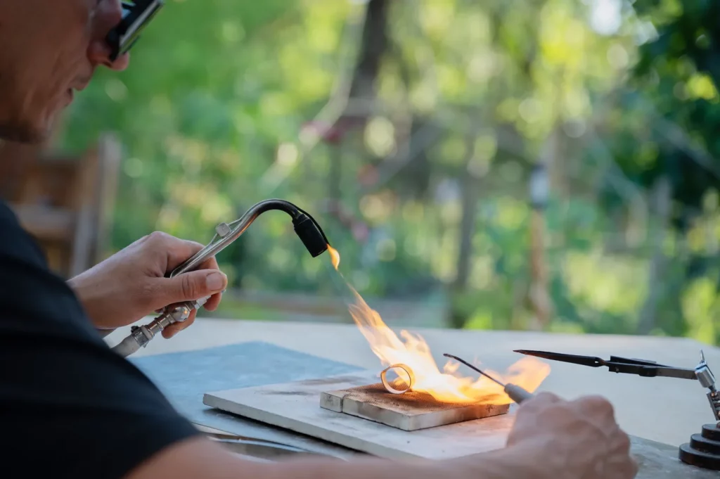 alt="Artisan bijoutier chauffant une bague en argent au chalumeau – Atelier Fusyom Île d’Oléron"